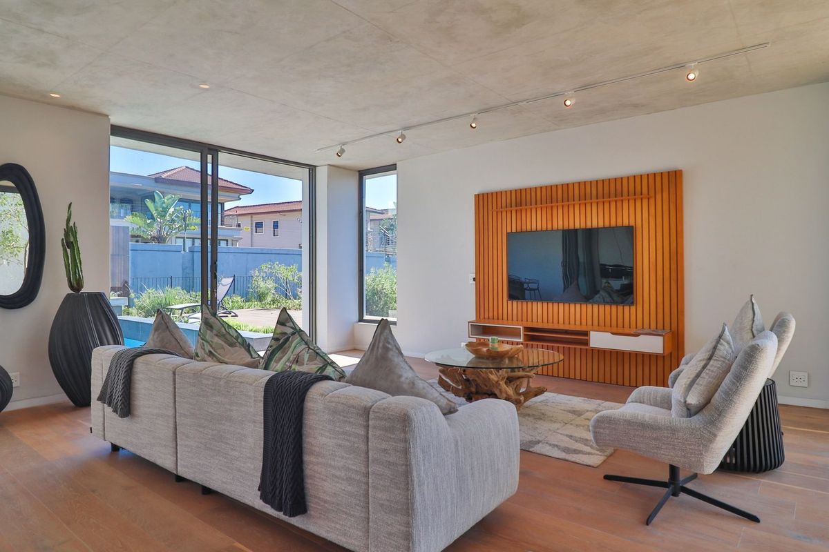 Modern living room featuring an exposed concrete ceiling, timber slat feature wall, and large sliding glass doors opening to the outdoor area.