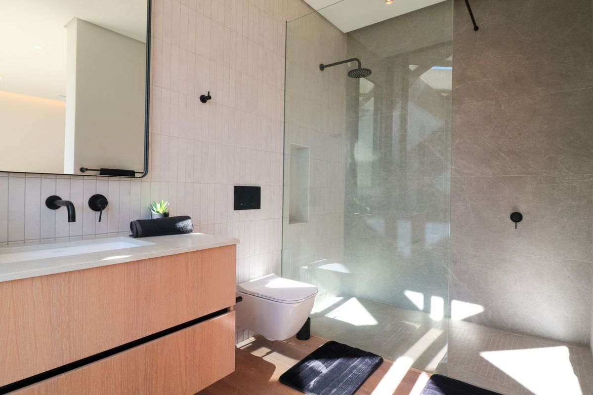 Modern bathroom featuring a wall-mounted vanity, wall-hung toilet, and a spacious walk-in shower with a glass screen and rain shower head.