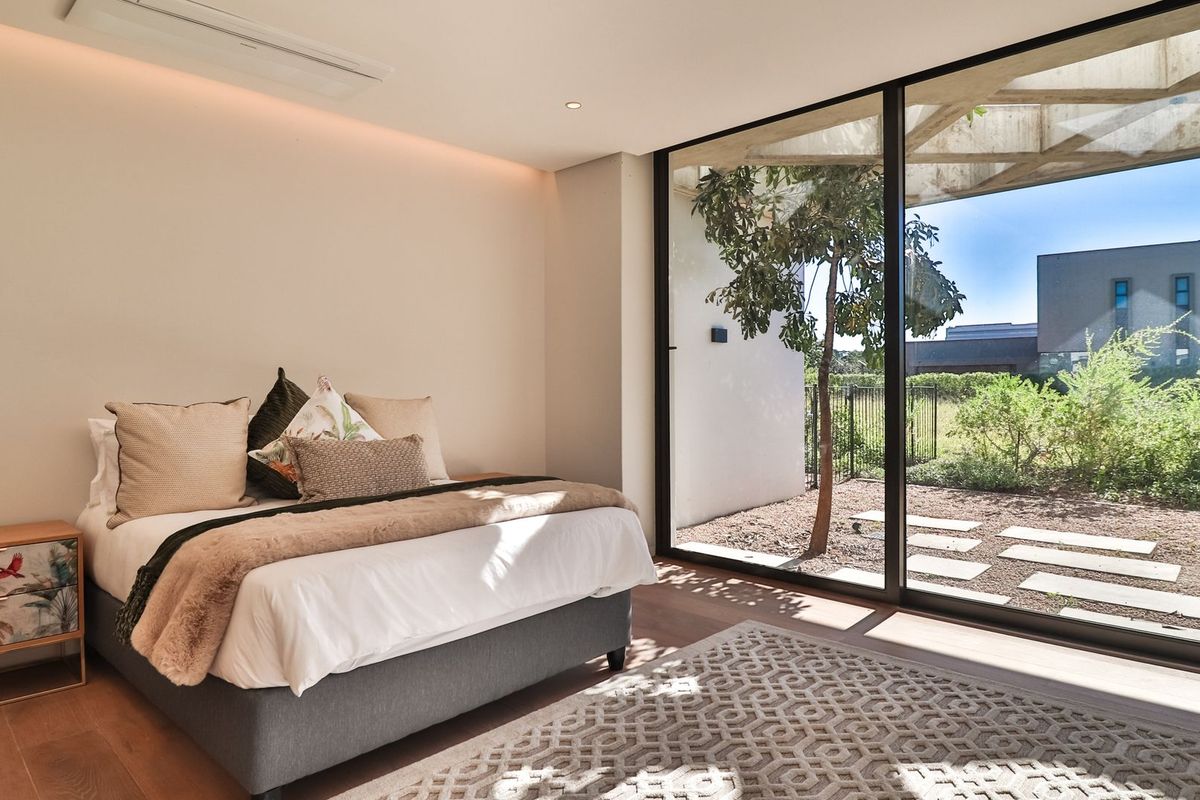 Modern bedroom featuring floor-to-ceiling sliding glass doors that open to a private garden area, complemented by recessed lighting and sleek hardwood flooring.