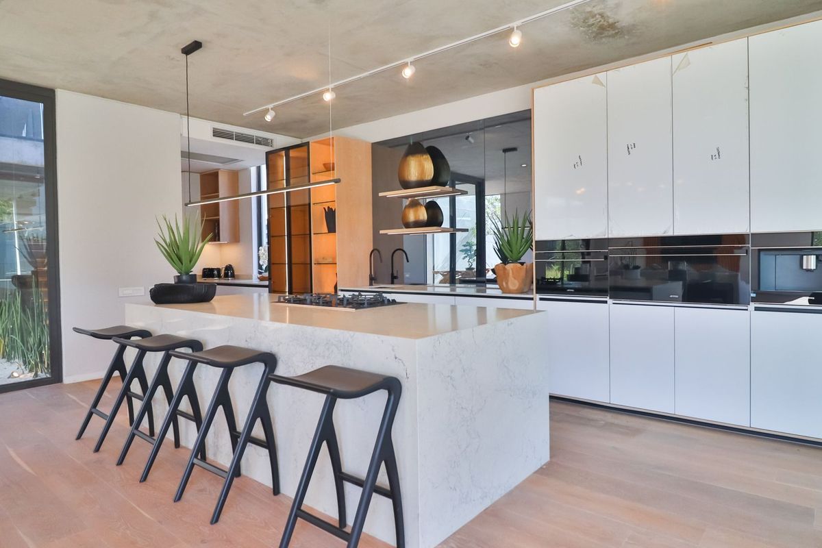 Modern kitchen featuring a stone island, integrated appliances, sleek cabinetry, track lighting, and timber flooring, opening to an outdoor area.