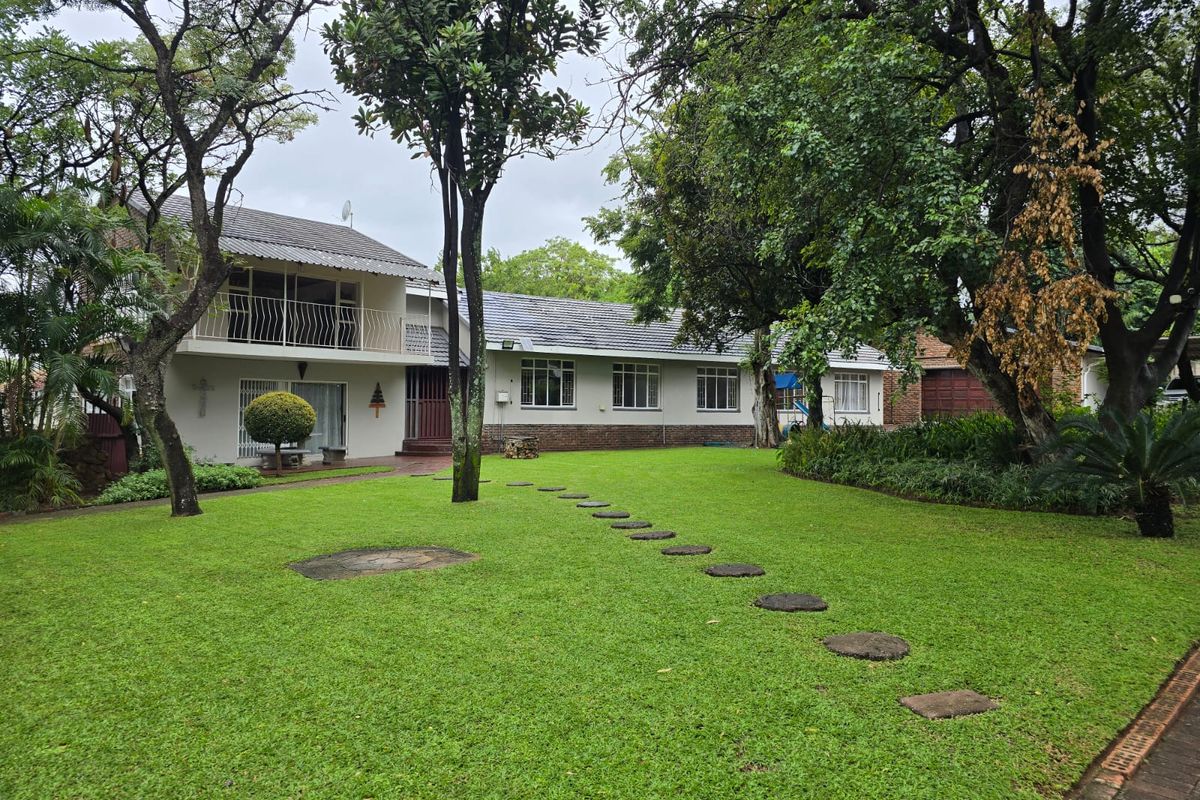 A spacious rear garden featuring a well-maintained lawn, mature trees, and a two-story house with a balcony and tiled roof.