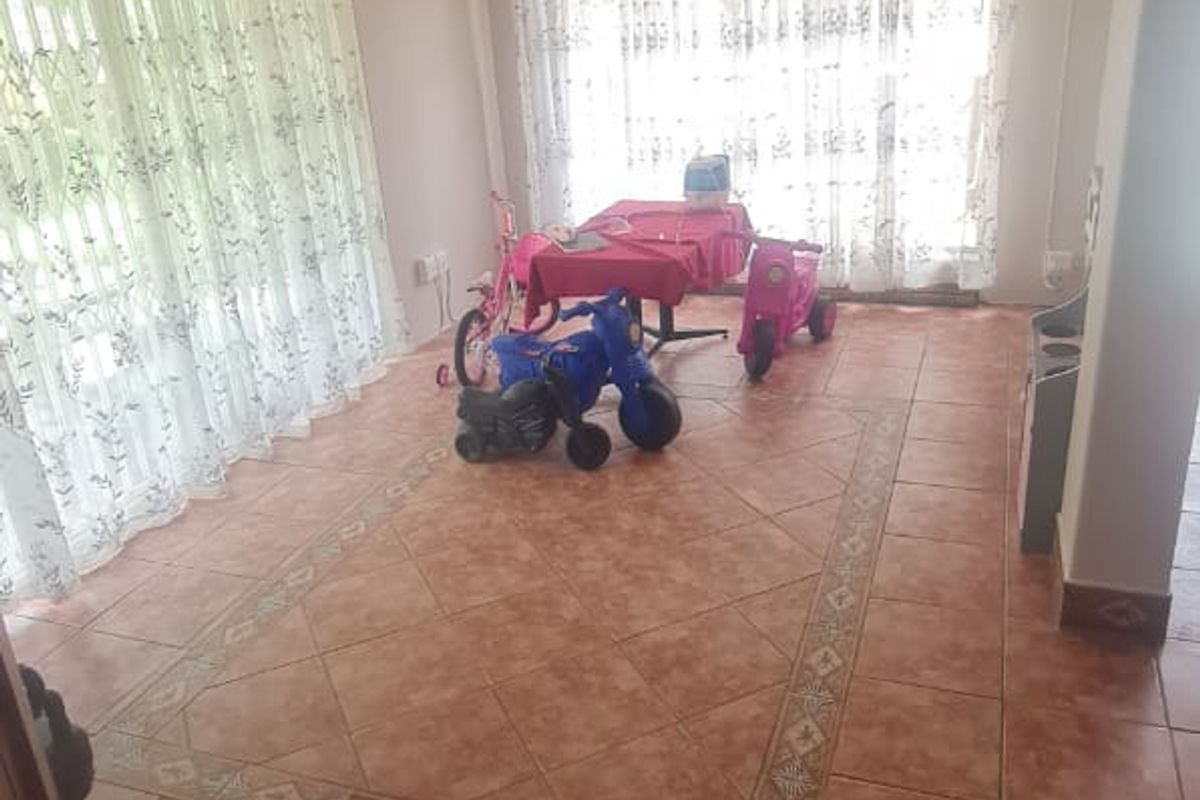 A spacious living area featuring terracotta-style tiled flooring with a decorative border and large sliding glass doors providing ample natural light.