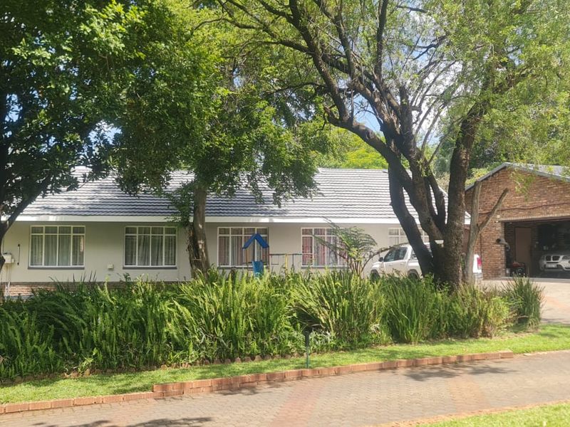 Front view of a single-story residence featuring a tiled roof, established garden, and a detached brick garage with a paved driveway.
