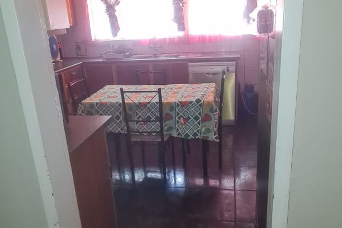 A functional kitchen space featuring tiled flooring, built-in cabinetry, and a tiled backsplash, viewed from an adjacent room.