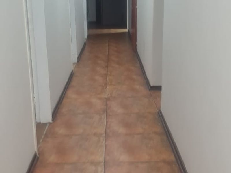 A long, empty residential hallway featuring neutral walls, tiled flooring, and recessed ceiling lighting, providing access to multiple rooms.