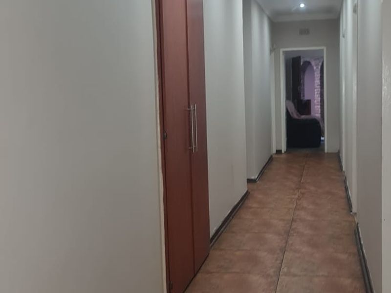 A long, neutral-toned hallway featuring tiled flooring, recessed ceiling lighting, and a built-in storage cupboard.
