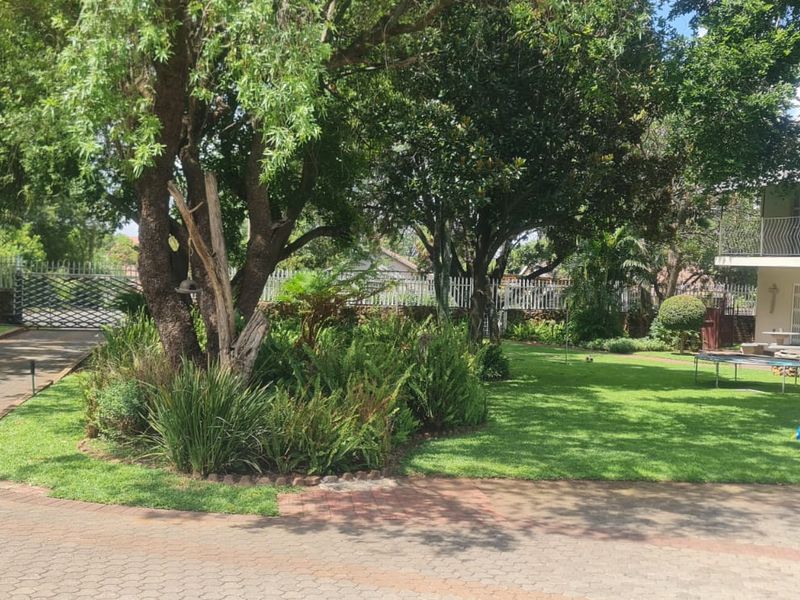 A spacious, well-maintained garden featuring a paved driveway, mature trees, and established landscaping surrounding the property.