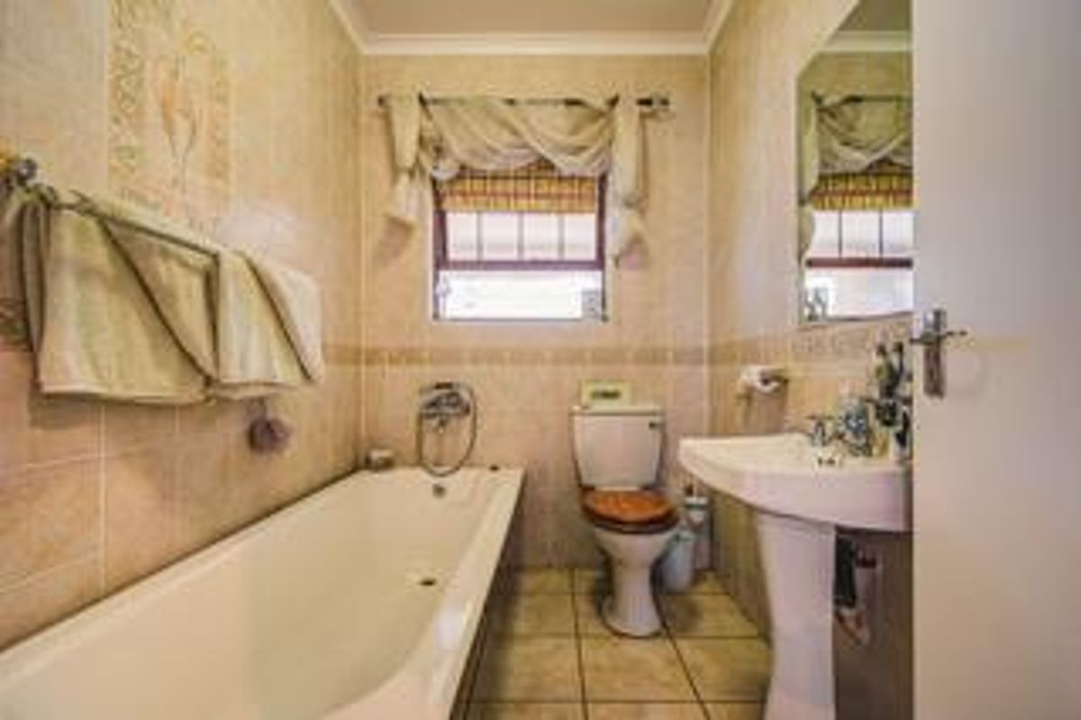 A functional bathroom featuring a bathtub, pedestal basin, and toilet, finished with neutral wall tiles and tiled flooring.