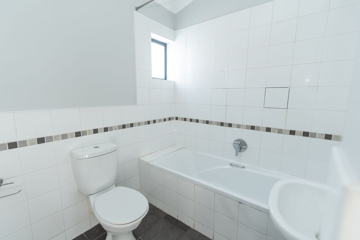 A functional bathroom featuring a white bathtub, wall-mounted toilet, and tiled walls with a decorative mosaic border.