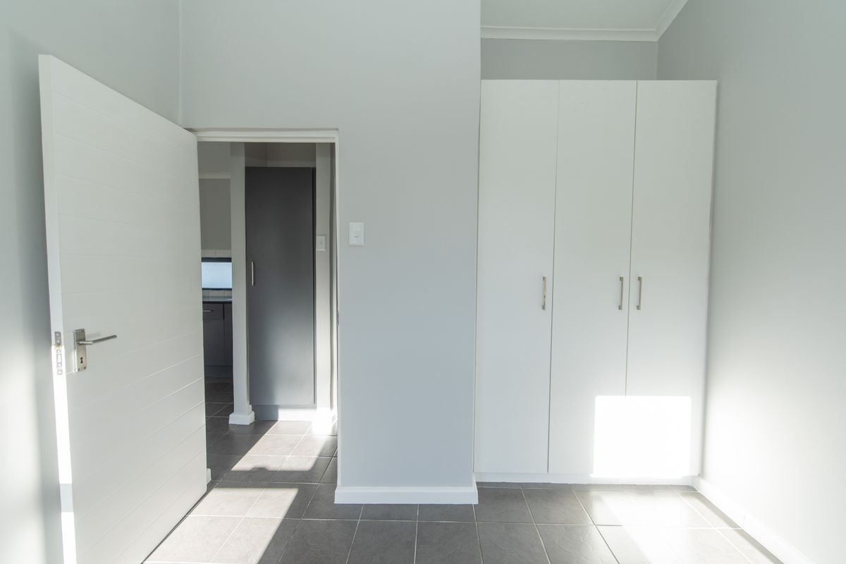 A clean, neutral-toned room featuring built-in white cabinetry and tiled flooring, with a doorway leading to an adjacent space.