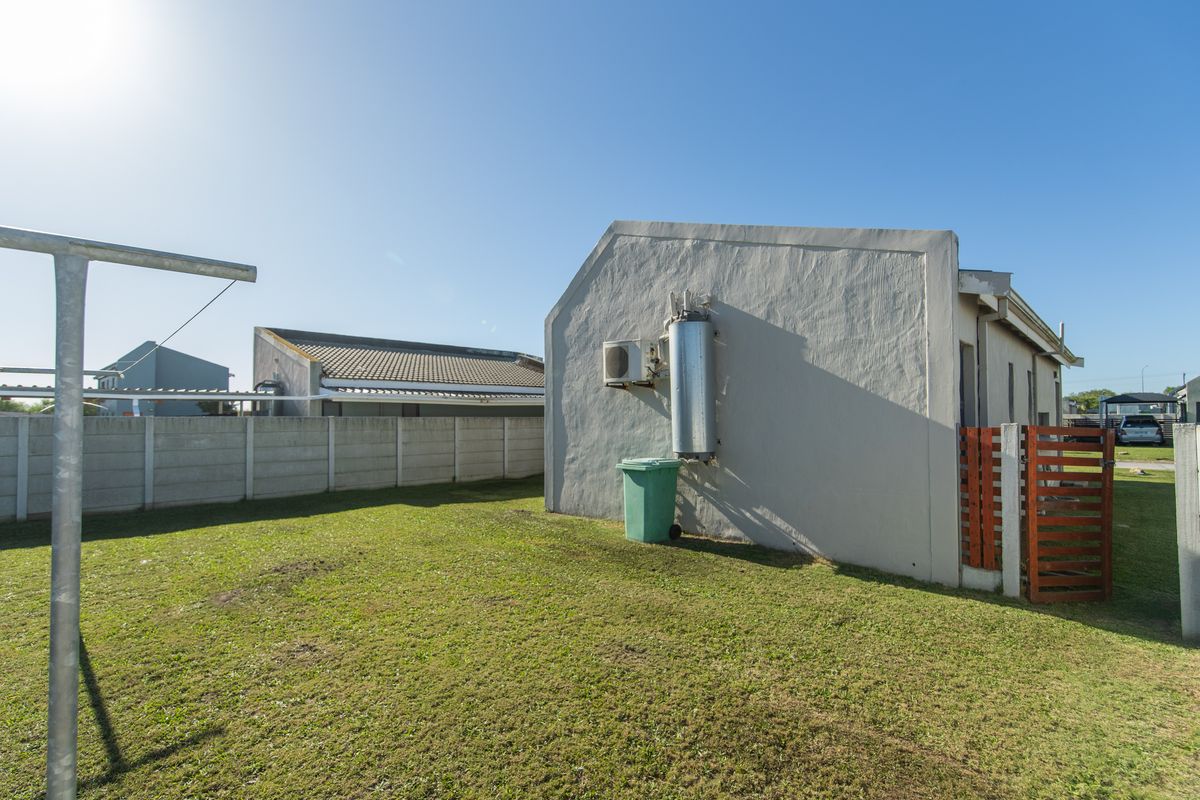 A view of the rear exterior of the house, featuring a lawn, boundary wall, and external water heating unit.