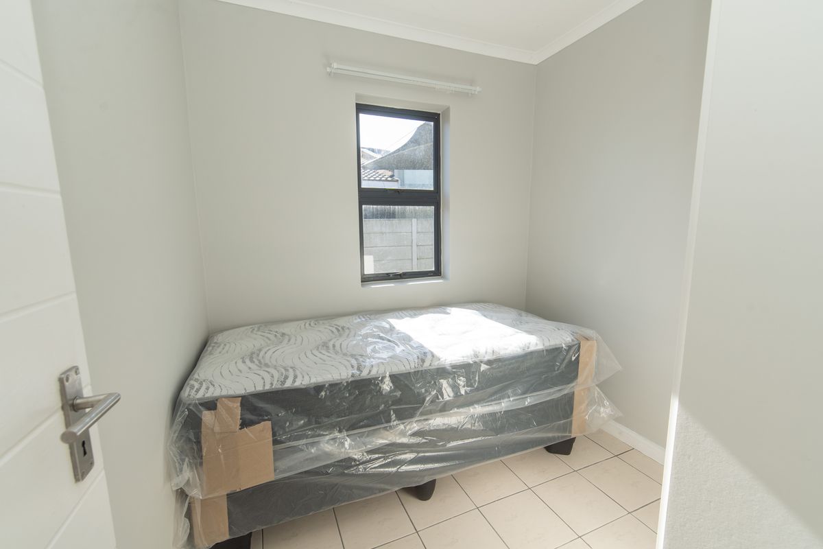 A compact bedroom featuring neutral wall paint, tiled flooring, and a single window providing natural light.