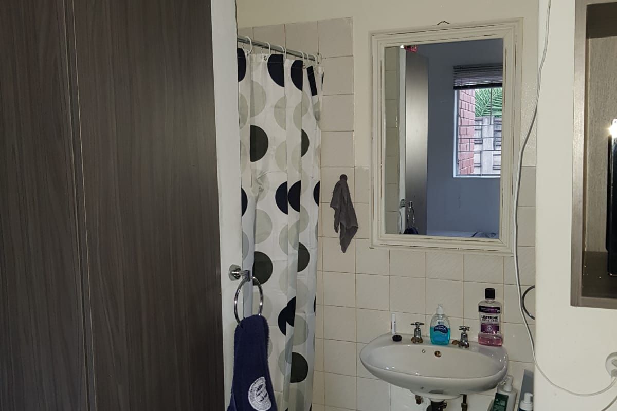 A functional bathroom featuring a pedestal washbasin, shower area with curtain, and wall-mounted mirror, requiring some cosmetic updates to improve its overall condition.