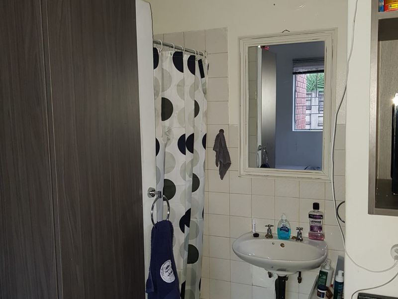 A functional bathroom featuring a pedestal washbasin, shower area with curtain, and wall-mounted mirror, requiring some cosmetic updates to improve its overall condition.