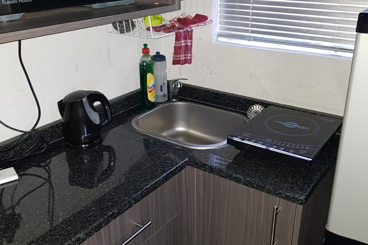 Compact kitchen area featuring dark wood-look cabinetry, granite countertops, and a stainless steel sink, suitable for a small apartment or studio unit.