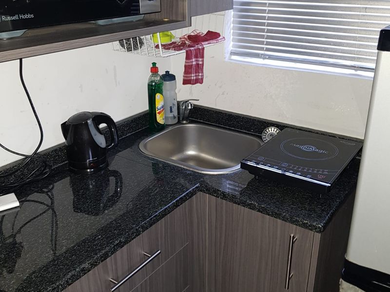 Compact kitchen area featuring dark wood-look cabinetry, granite countertops, and a stainless steel sink, suitable for a small apartment or studio unit.