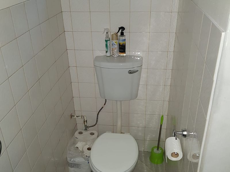A compact bathroom featuring ceramic wall and floor tiles, a standard toilet, and a small high-level window for ventilation.