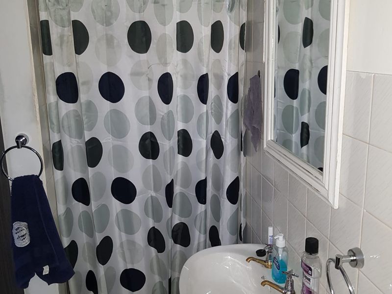 A compact bathroom featuring a wall-mounted basin, tiled walls, and a shower area with a curtain.