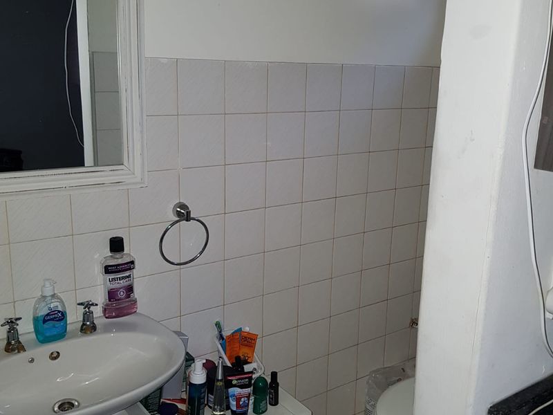 A compact bathroom featuring a pedestal basin, wall-mounted mirror, and tiled walls, requiring minor cosmetic updates to improve the overall finish.