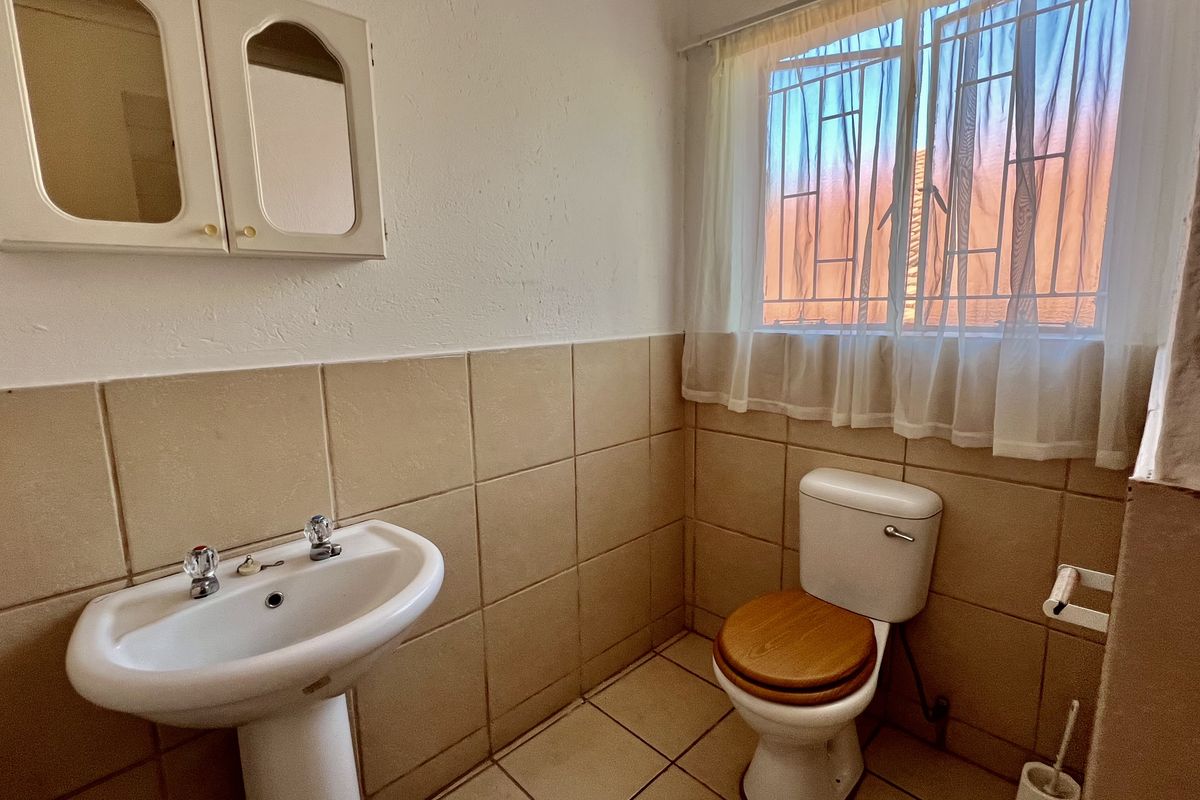 A functional bathroom featuring a pedestal basin, wall-mounted medicine cabinet, and a standard toilet with tiled walls and flooring.