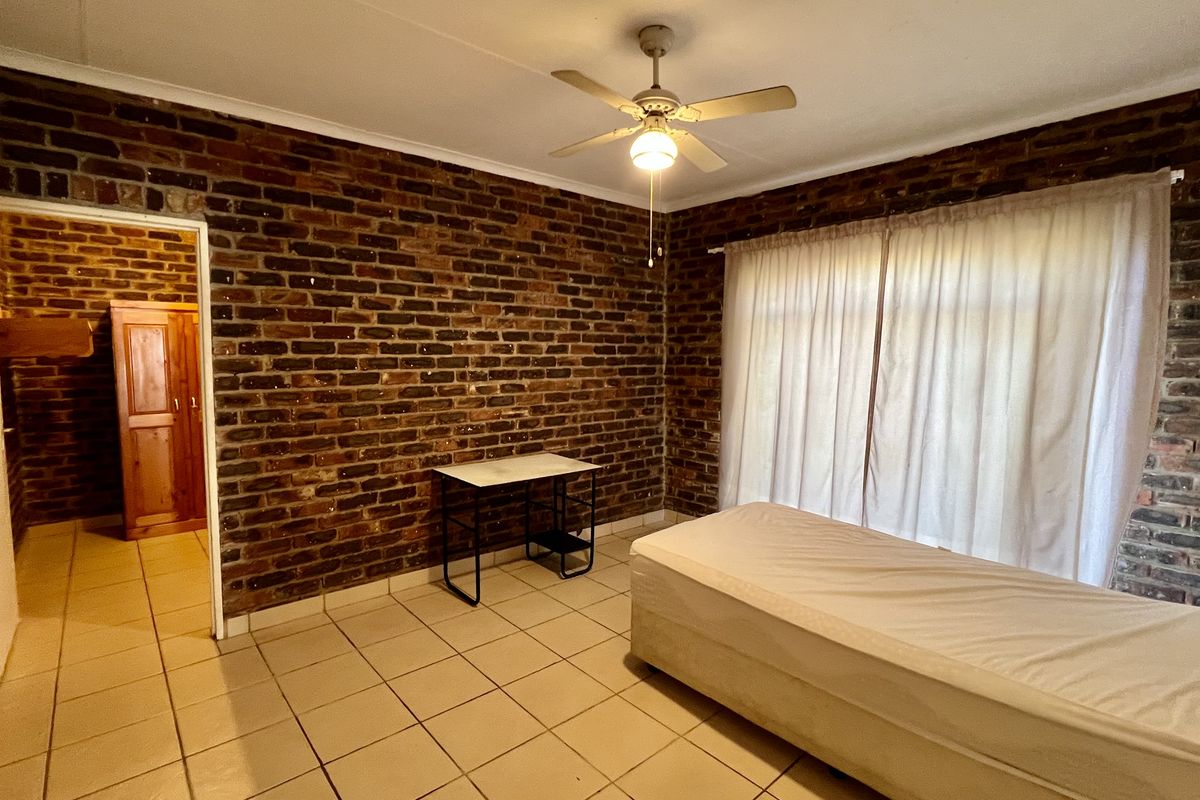 A bedroom featuring exposed brick walls, tiled flooring, and a ceiling fan, offering a rustic aesthetic with direct access to an adjoining space.