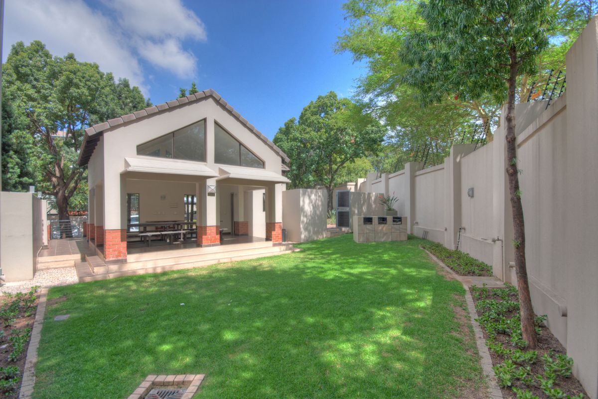 A well-maintained rear garden featuring a covered patio area, built-in braai, and perimeter walling, providing a private outdoor space.