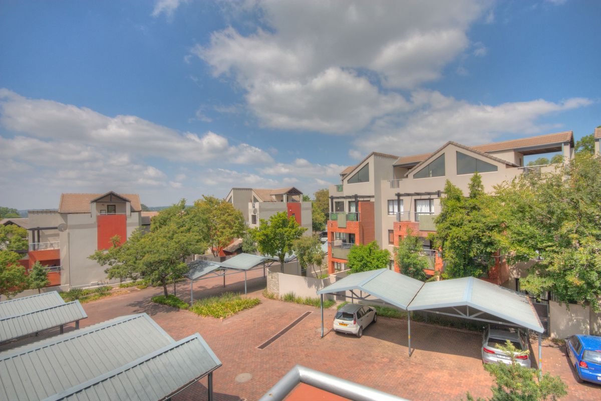 An elevated view of the apartment complex grounds, featuring paved parking areas with covered carports and established landscaping between the residential buildings.