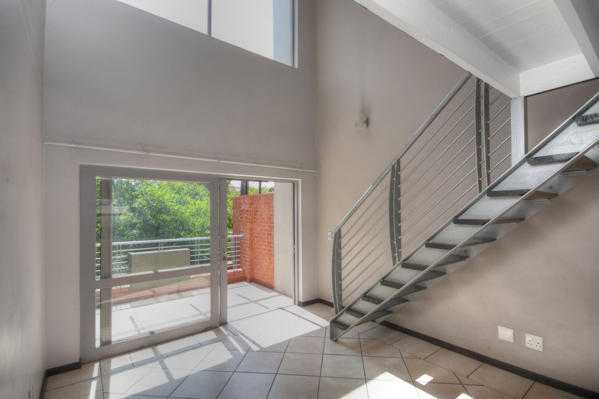 Bright double-volume living area featuring a modern metal staircase, tiled flooring, and large sliding glass doors opening onto a private balcony.