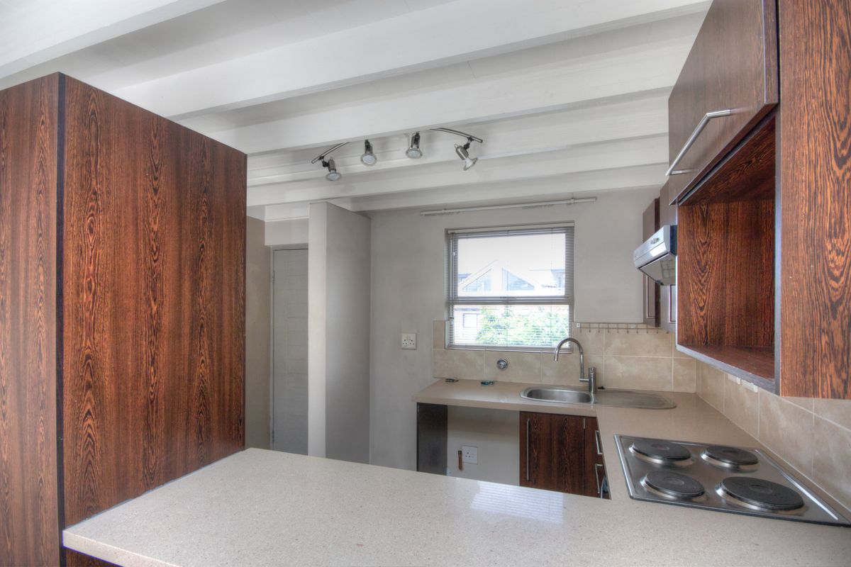 A functional kitchen featuring dark wood-grain cabinetry, stone-look countertops, a built-in electric hob, and an integrated extractor fan under exposed white ceiling beams.