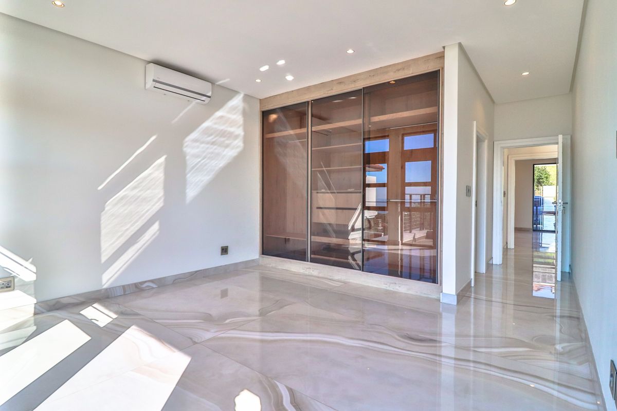 A bright, modern bedroom featuring high-end marble-look floor tiles, a large built-in wardrobe with glass doors, and a wall-mounted air conditioning unit.