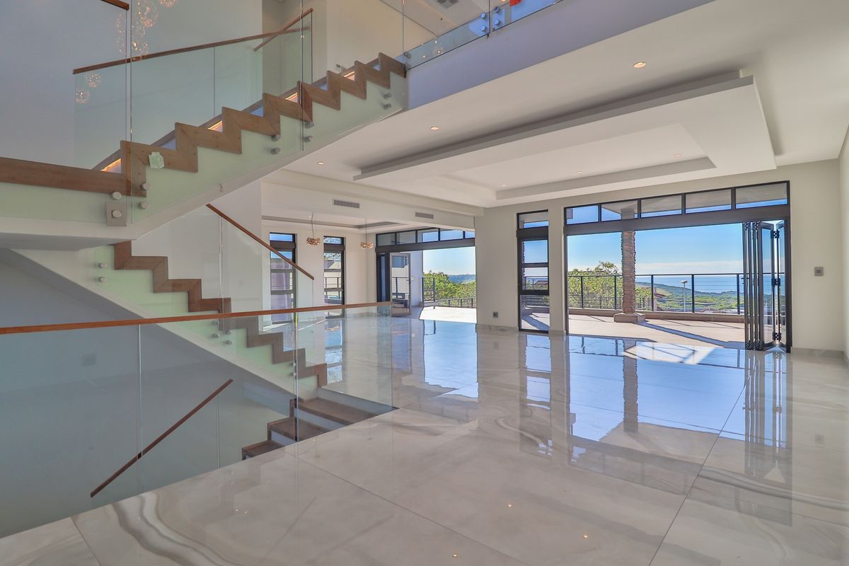 Spacious open-plan living area featuring a modern floating staircase, glass balustrades, polished porcelain tiles, and large bi-fold doors opening to a scenic balcony.