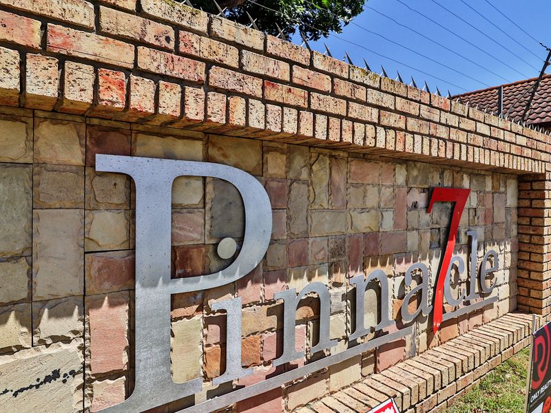 A close-up view of the brick and stone-clad entrance wall featuring the Pinnacle 7 complex signage and security spikes.