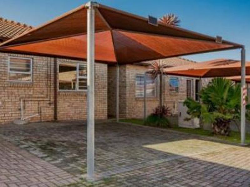 A paved driveway area featuring a permanent shade cloth carport structure attached to a facebrick townhouse exterior.