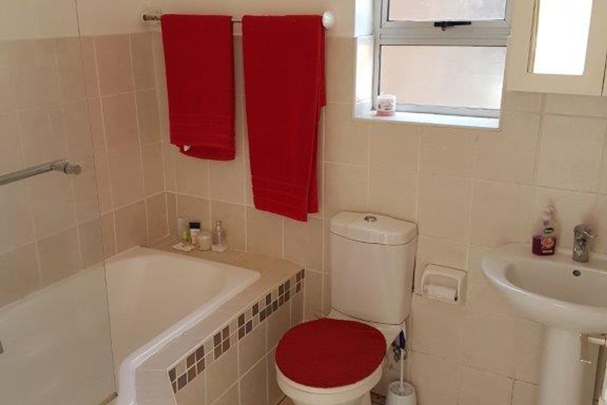 A functional bathroom featuring a bathtub with a glass screen, pedestal basin, and tiled finishes throughout.