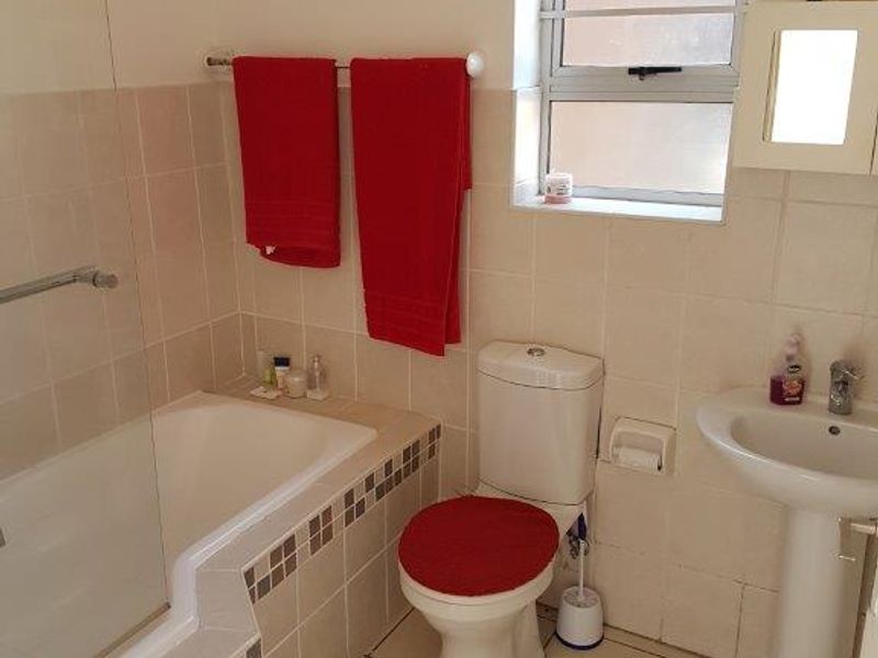 A functional bathroom featuring a bathtub with a glass screen, pedestal basin, and tiled finishes throughout.