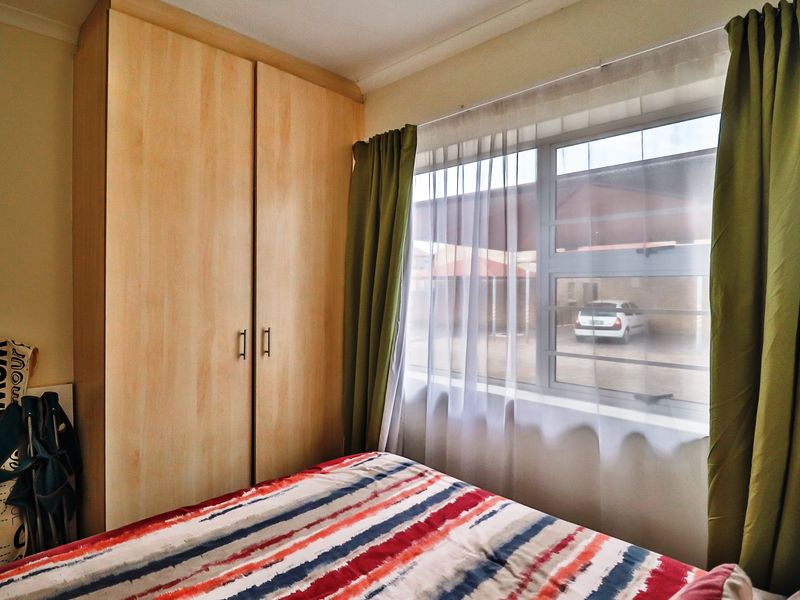A bedroom featuring a built-in wooden wardrobe and a window with views of the exterior parking area.