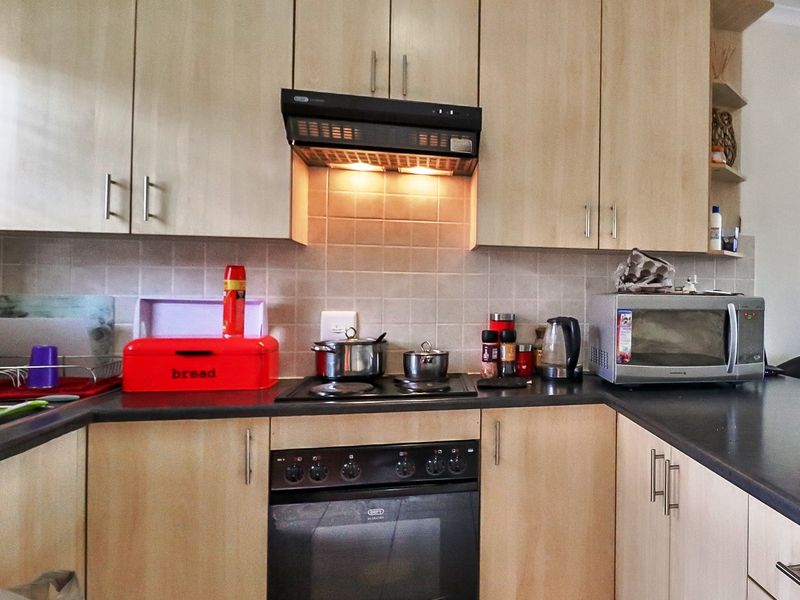 A functional kitchen featuring light wood-finish cabinetry, dark countertops, a built-in oven with hob, and a tiled backsplash.