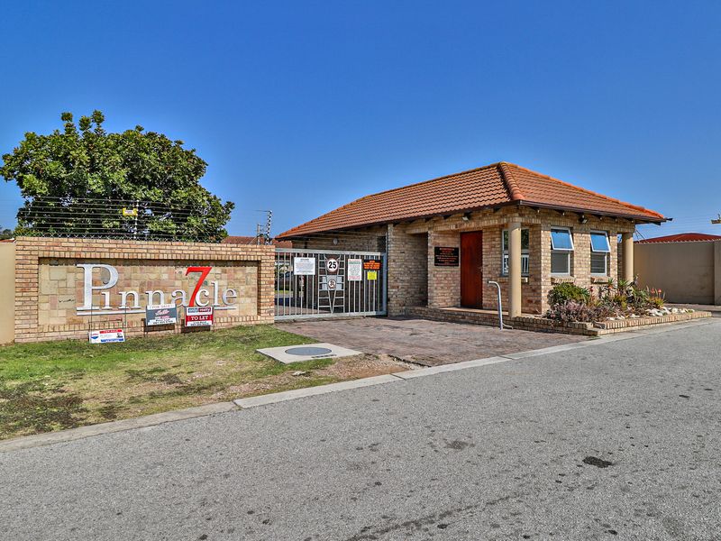 The front entrance of the Pinnacle 7 townhouse complex, featuring a brick facade, security gate, and paved driveway access.