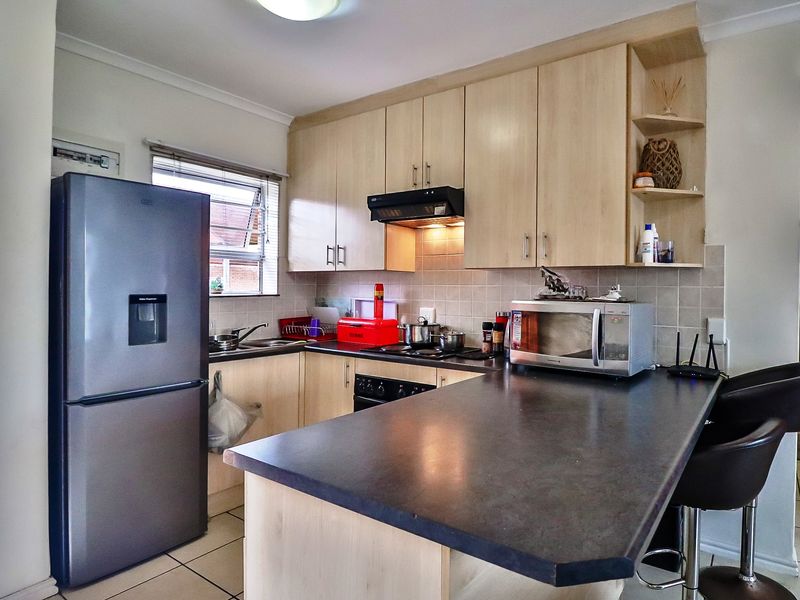 A functional kitchen featuring light wood-finish cabinetry, dark laminate countertops, tiled backsplash, and integrated cooking appliances with a breakfast bar area.