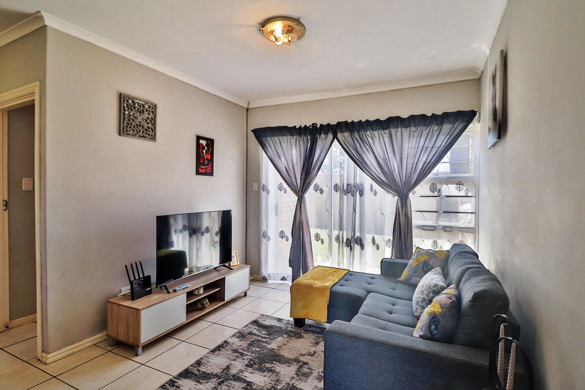 A comfortable living room featuring tiled flooring, cove cornicing, and a sliding glass door providing natural light and access to the exterior.