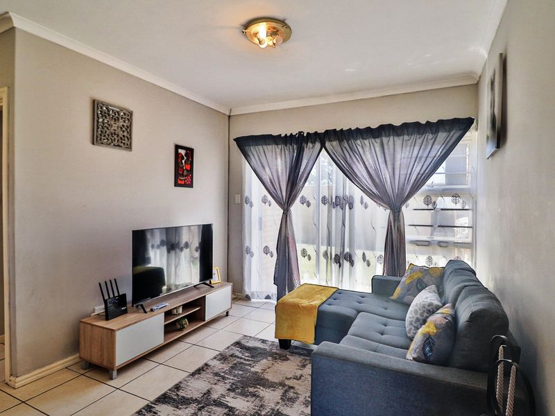 A comfortable living room featuring tiled flooring, cove cornicing, and a sliding glass door providing natural light and access to the exterior.