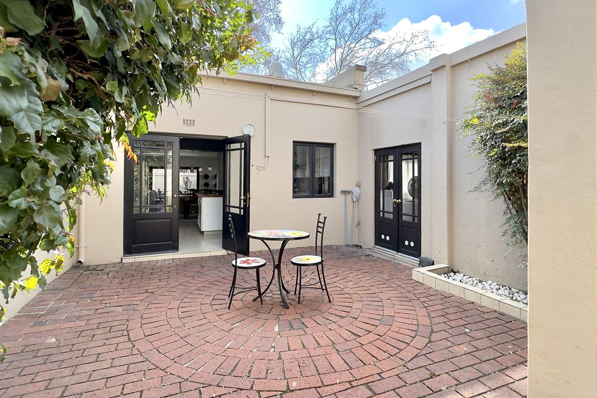 A private rear courtyard featuring classic red brick paving, established greenery, and double-door access to the interior living spaces.