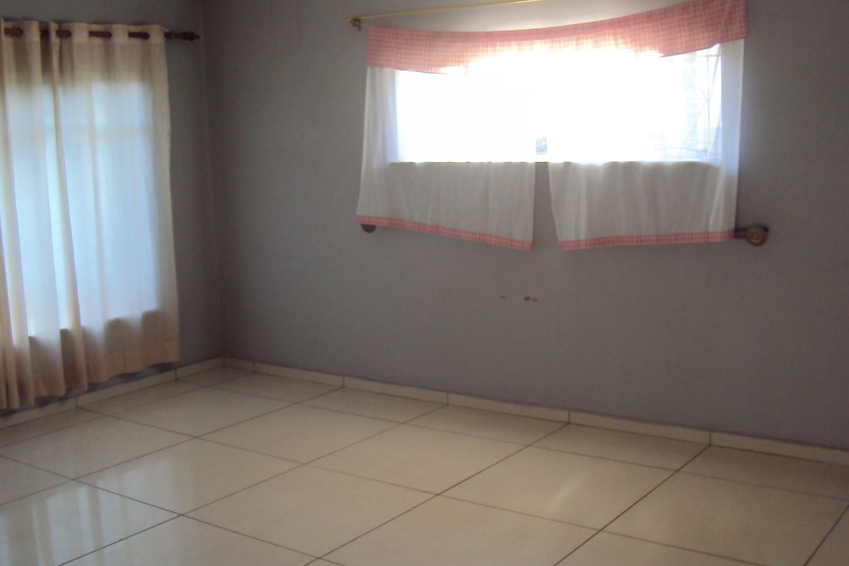 A bright, empty bedroom featuring neutral tiled flooring and large windows, providing a clean and versatile space ready for personalization.