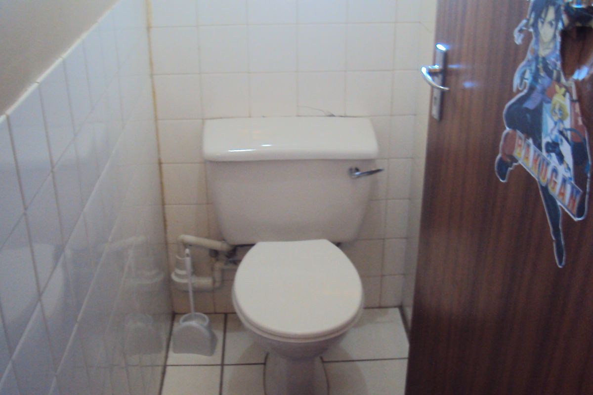 A compact bathroom featuring a standard white toilet, tiled walls, and tiled flooring.