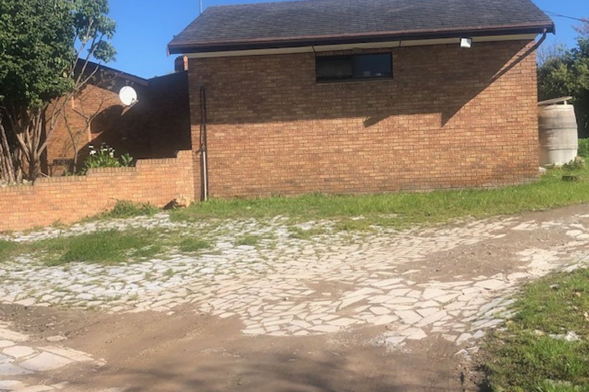 Rear exterior view of the property featuring a brick building, stone paved driveway, and a water tank set within a rural small holding landscape.