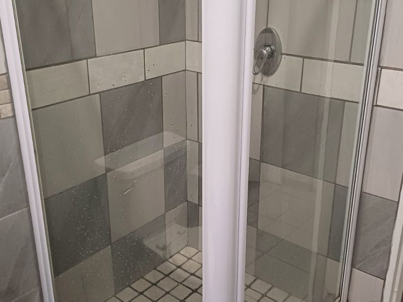 A functional bathroom featuring a glass-enclosed shower with modern grey and white wall tiling and a standard toilet.
