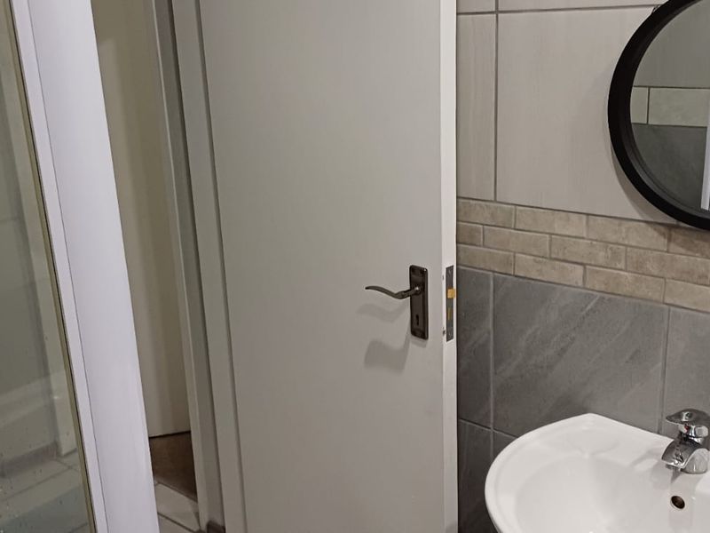 A functional bathroom featuring a shower enclosure, pedestal basin with mixer tap, and neutral wall tiling.