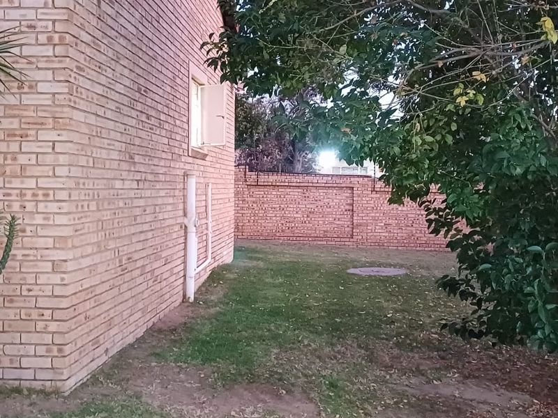 A view of the rear exterior of the townhouse, featuring face brick walls, a lawn area, and a perimeter boundary wall.