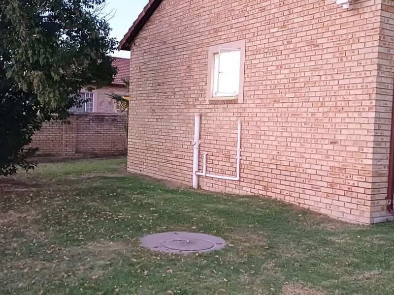 A view of the rear exterior of the townhouse, featuring a face brick facade, external plumbing, and a grassed garden area.