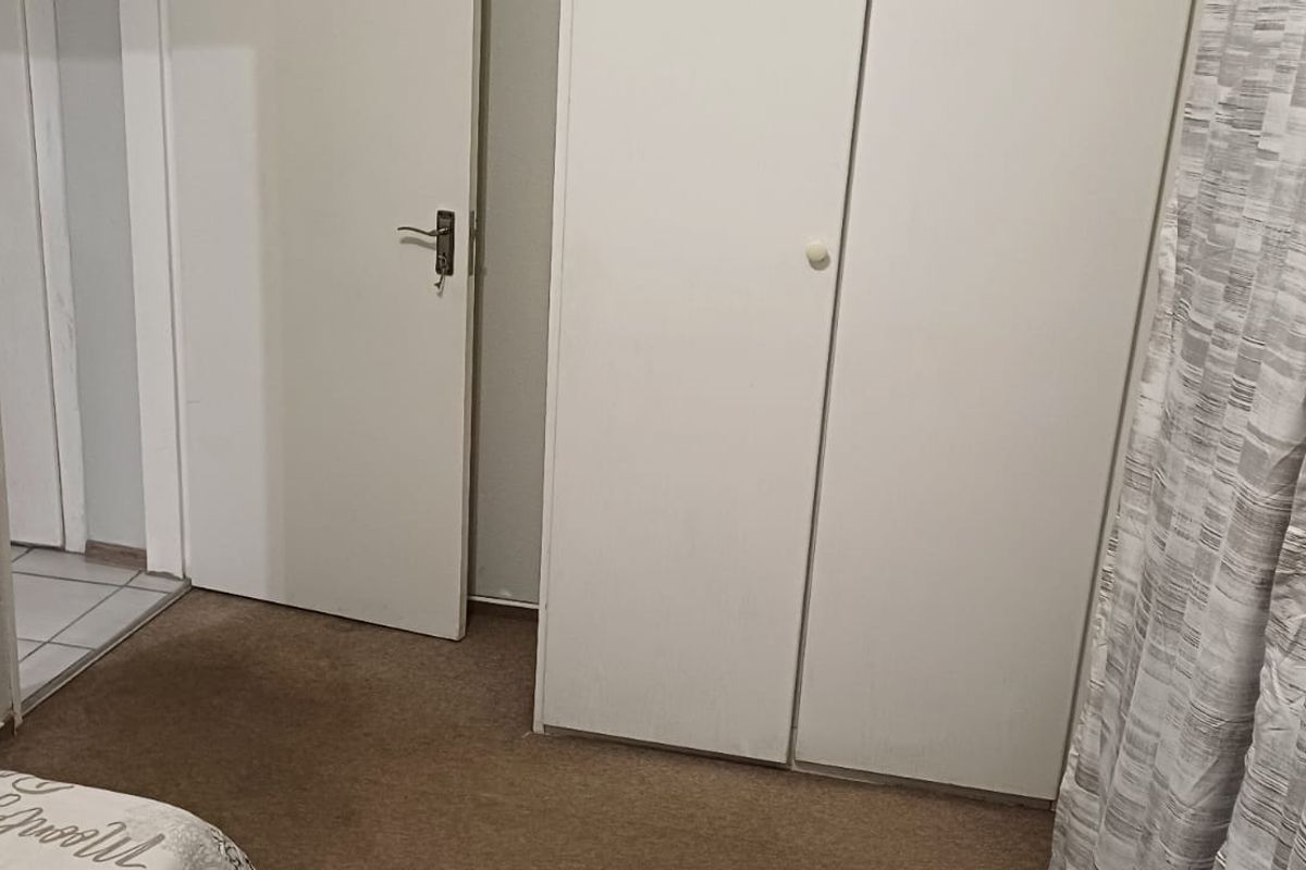A bedroom featuring built-in wardrobe storage, carpeted flooring, and access to an adjacent hallway.